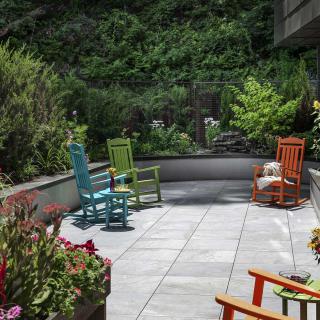 A peaceful patio with colorful rocking chairs surrounded by lush garden greenery.