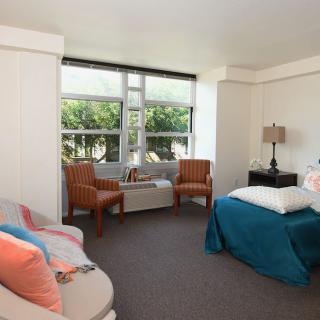 A cozy bedroom with modern furnishings and natural light streaming through a large window.