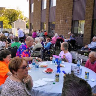 A lively outdoor community gathering with seniors enjoying food and conversation.