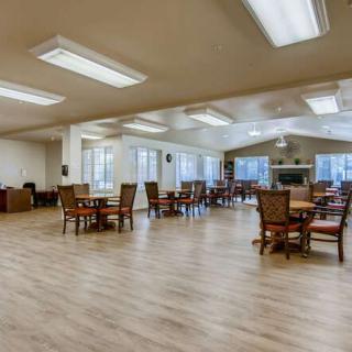 A spacious dining area with wooden tables and chairs, featuring large windows and wood flooring.
