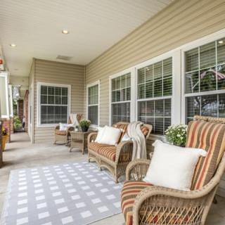 A cozy porch featuring wicker chairs with cushions and a patterned rug.