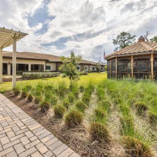 A scenic garden with lush greenery, a brick pathway, and a gazebo in the background.