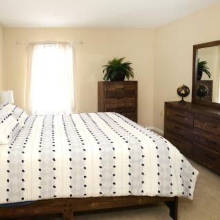 A minimalist bedroom with a neatly made bed, dresser, and mirror.