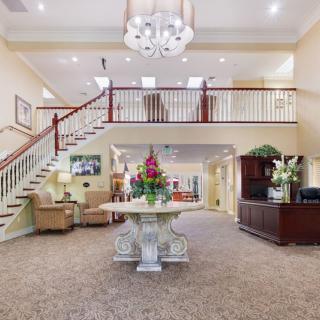 A well-lit lobby featuring a grand staircase, reception desk, and decorative flowers.