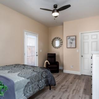 A cozy bedroom featuring a bed, chair, mirror, and ceiling fan with wood flooring.
