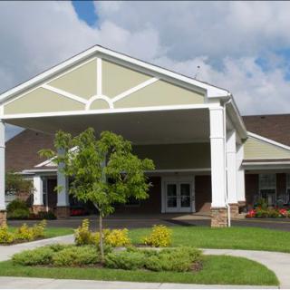 A building entrance with landscaped greenery and a cloudy sky.