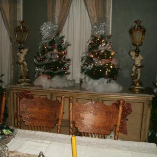 A dining room with ornate furniture, decorated with miniature Christmas trees and elegant lamps.