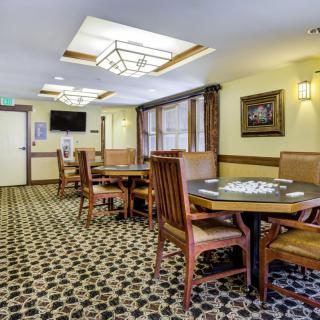 A cozy dining area with wooden tables and chairs, featuring patterned carpet and soft lighting.