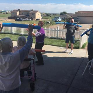 A group of seniors participating in an outdoor exercise class with foam noodles.