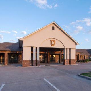 A building with a prominent entrance and parking lot, set against a partly cloudy sky.