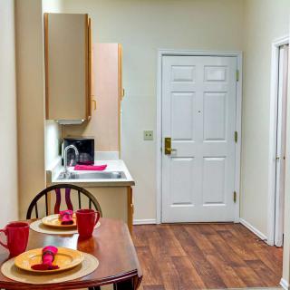 A small kitchen and dining area with a wooden floor, featuring a table set with dishes and a view of the entrance door.