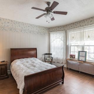 A cozy bedroom featuring a wooden bed, ceiling fan, and large windows with natural light.