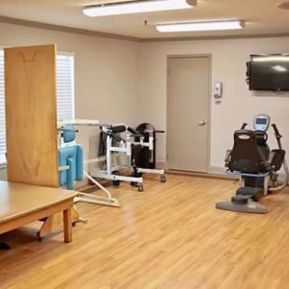 A compact fitness room with various exercise equipment and a wall-mounted TV.