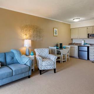 A cozy living space with a blue sofa and patterned armchair adjacent to a small kitchenette.