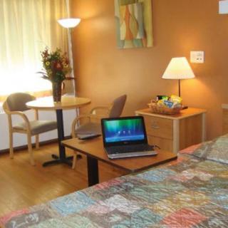 A cozy hotel room with a laptop on the table and a bed nearby.