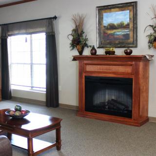 A cozy living room with a wooden fireplace and framed artwork above, featuring comfortable seating and decor.