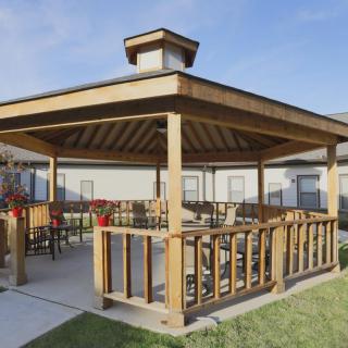 A wooden gazebo with seating area, situated in a landscaped outdoor setting.