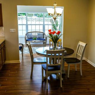 A cozy dining area with a round table and chairs, leading to a sunlit room adorned with tulips and wooden flooring.