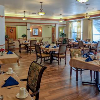 A well-lit dining room with neatly arranged tables and chairs, featuring elegant table settings on a wooden floor.