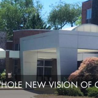 Modern building entrance with landscaped surroundings and a slogan.
