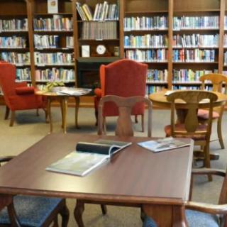 A cozy library reading area with bookshelves, tables, and comfortable armchairs.