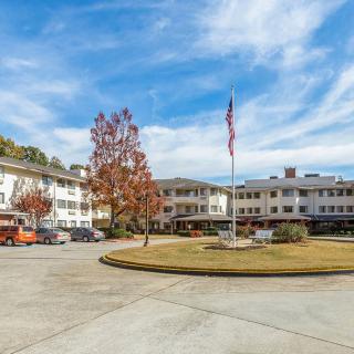 A large building surrounded by a parking lot with a flagpole and trees, under a partly cloudy sky.