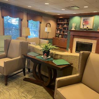 A warm and inviting lounge area featuring comfortable seating, a small table with a plant, and a bookshelf in the background.