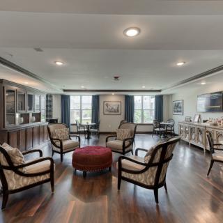 A spacious living room with elegant furniture arranged around a central ottoman and large windows letting in natural light.