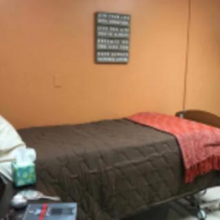 A cozy bedroom with an orange wall and a neatly made single bed featuring a brown bedspread and an orange throw.