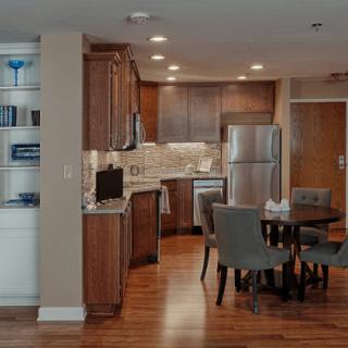 A modern kitchen and dining area with wooden cabinets, stainless steel appliances, and a wood floor.