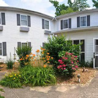 A charming house with a lush garden in front, featuring vibrant flowers and greenery.