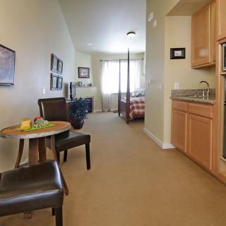 A cozy apartment interior featuring a kitchenette, a small seating area, and a view into the bedroom.