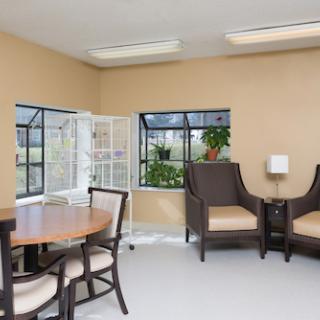 A cozy seating area featuring a round table and comfortable chairs, illuminated by natural light from large windows.