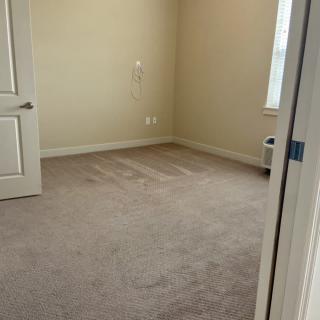 An empty room with beige walls, a carpeted floor, an open door, and a window.