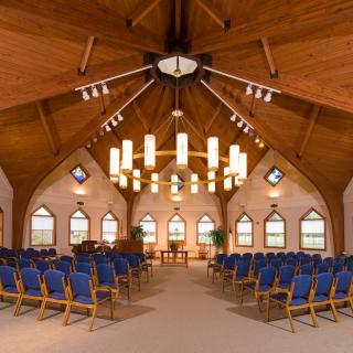 An interior view of a church with wooden ceilings, blue seating, and elegant lighting fixtures.