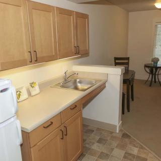 A compact kitchen and dining area in an apartment, featuring wooden cabinets and a countertop with a sink.