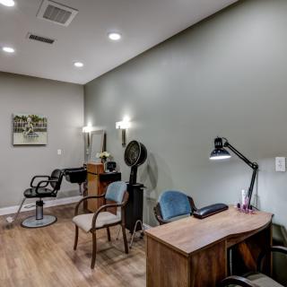 A cozy salon interior featuring a desk, chairs, a hair dryer, and mirrors with soft lighting.