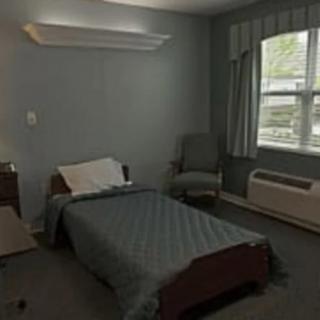 A minimalist bedroom with a single bed, chair, window, and air conditioner.