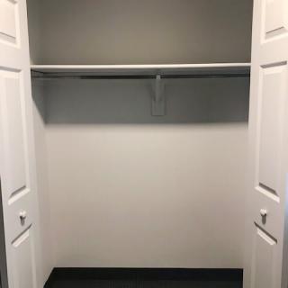 An empty white closet with open doors and a hanging rod.