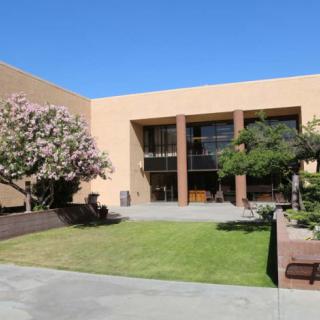 A modern building exterior with a landscaped lawn and trees under a clear blue sky.