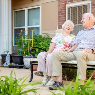 An elderly couple enjoying a moment together on a bench in their garden.