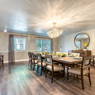 An elegantly designed dining room featuring a large table, multiple chairs, and a stunning chandelier, complemented by wood flooring and tasteful decor.