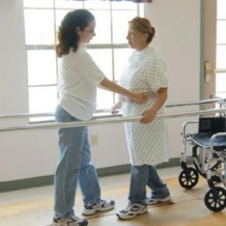 A healthcare professional assists a patient during a physical therapy session using parallel bars.