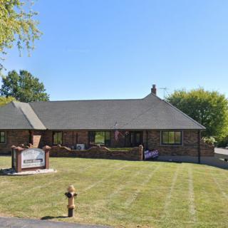A brick church building with a manicured lawn and trees in the background under a clear blue sky.