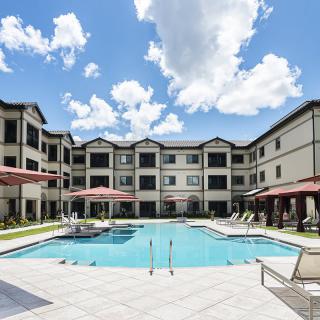 An outdoor swimming pool surrounded by a residential apartment complex on a sunny day.