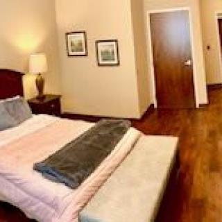 A cozy bedroom with a neatly made bed, wooden flooring, and ambient lighting.