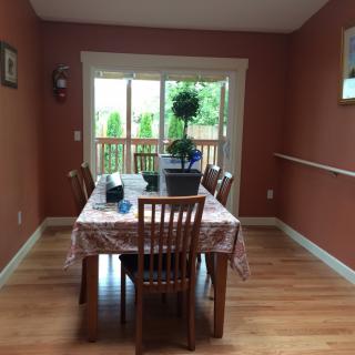 A dining room with a wooden table and chairs, featuring a plant centerpiece near a large window overlooking the outdoors.