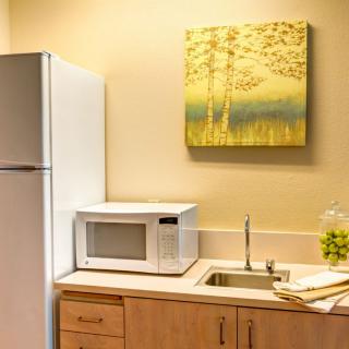 A small kitchen area featuring a refrigerator, microwave, sink, and artwork on the wall.