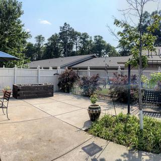 A sunny backyard patio featuring outdoor furniture, a garden with potted plants, and a surrounding fence.