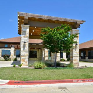 A building entrance featuring stone pillars, surrounded by landscaping and greenery under a clear blue sky.